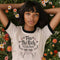 Off-white ringer t-shirt with black contrast trim on the collar and sleeve cuffs. The front features a hand-lettered design with the phrase "Tax the Rich, Feed the Poor, Pet the Cats", arranged in an elegant, whimsical script. Surrounding the text are small decorative elements, including hearts, stars, and delicate floral accents. Below the text, a simple, happy cat illustration with raised paws adds a playful and charming touch. The t-shirt has a vintage-inspired fit, made from soft cotton fabric with a sl